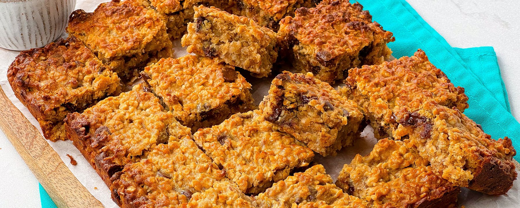 Golden oat bars with chocolate chips arranged on parchment paper with turquoise cloth