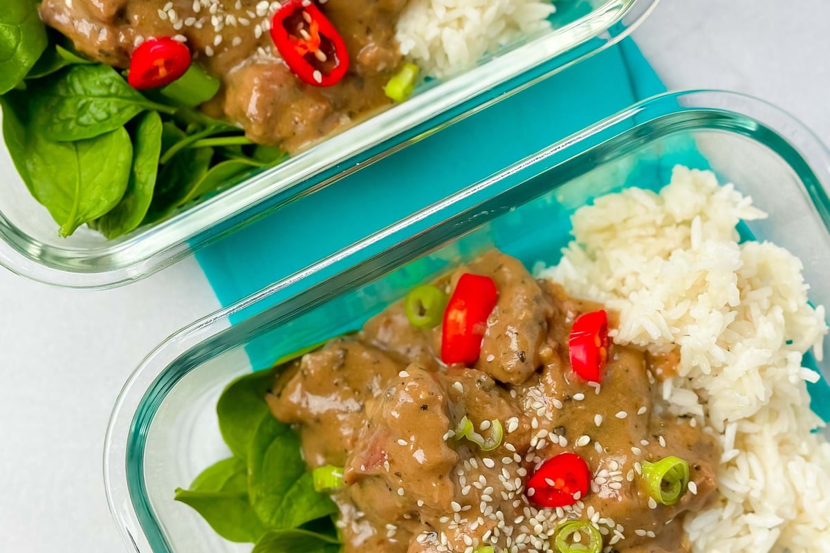 Two glass containers with rice, spinach, creamy sauce, red chili, spring onion, and sesame