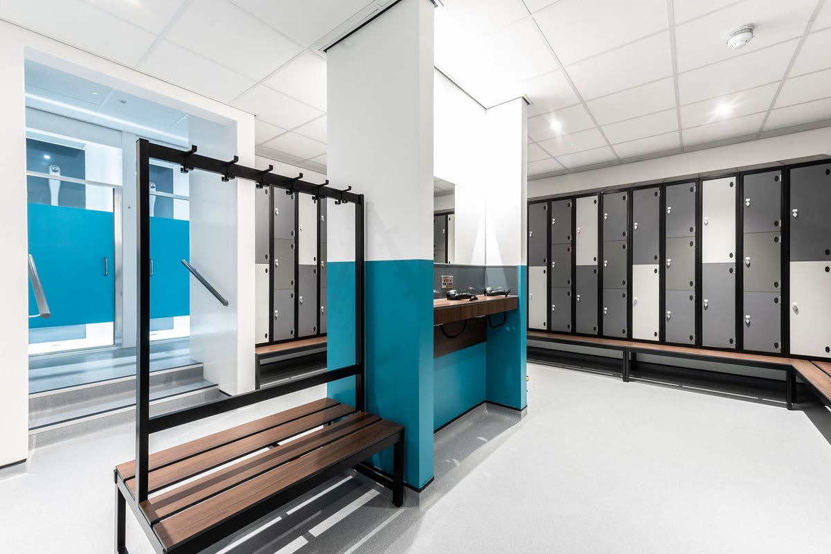 PureGym Milton Keynes Kingston Centre: Changing room cubicles, wooden benches, and lockers in blue and dark tones.