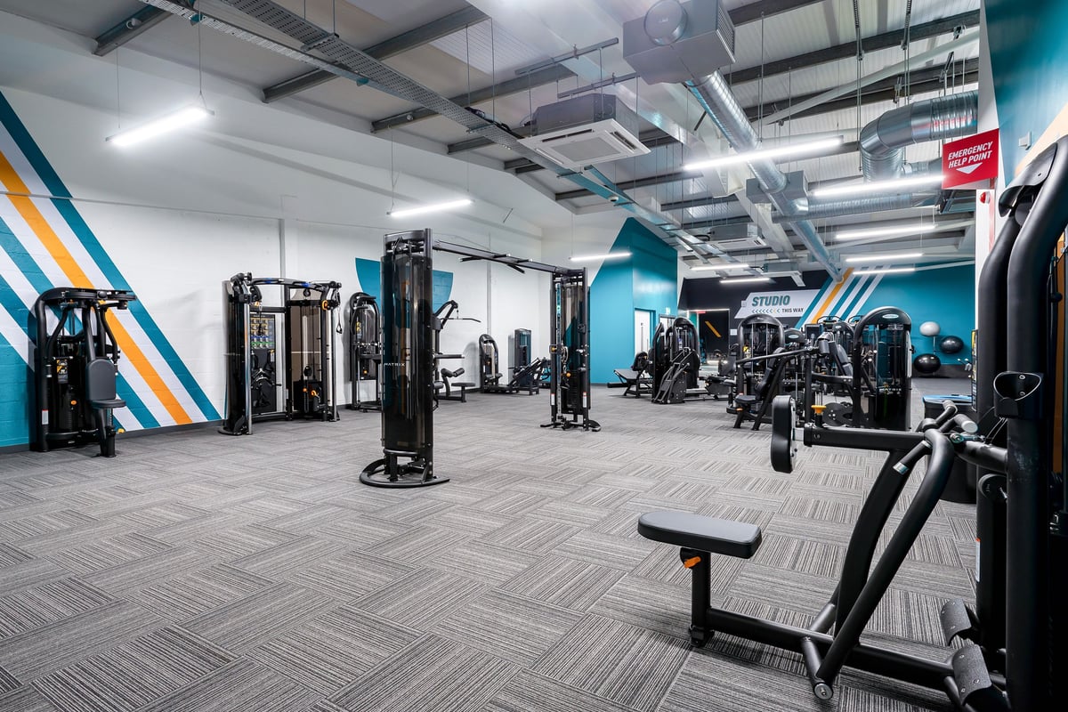 PureGym Stratford-upon-avon: Weight machines, cable stations, benches, and rubberized flooring in a gym with bright lighting.