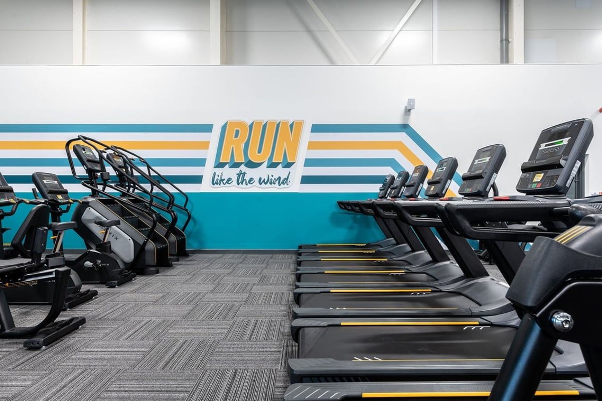 PureGym Portishead: Rows of treadmills and stationary bikes, colourful mural wall with "Run like the wind" motivational text.