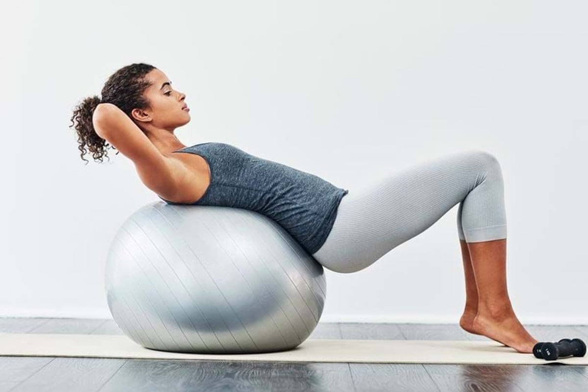 Woman doing back exercises on a silver stability ball on a yoga mat indoors