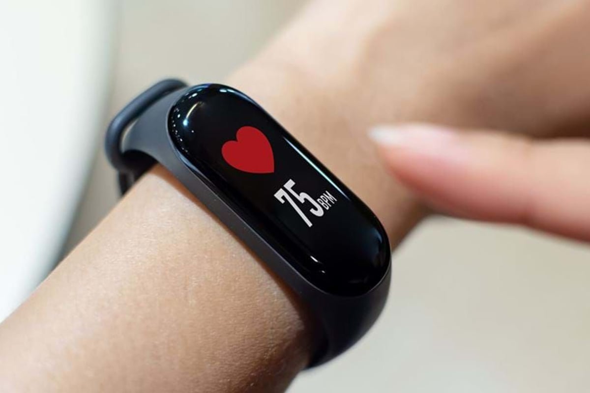 Fitness tracker on wrist showing heart rate of 75 bpm with finger pointing at it