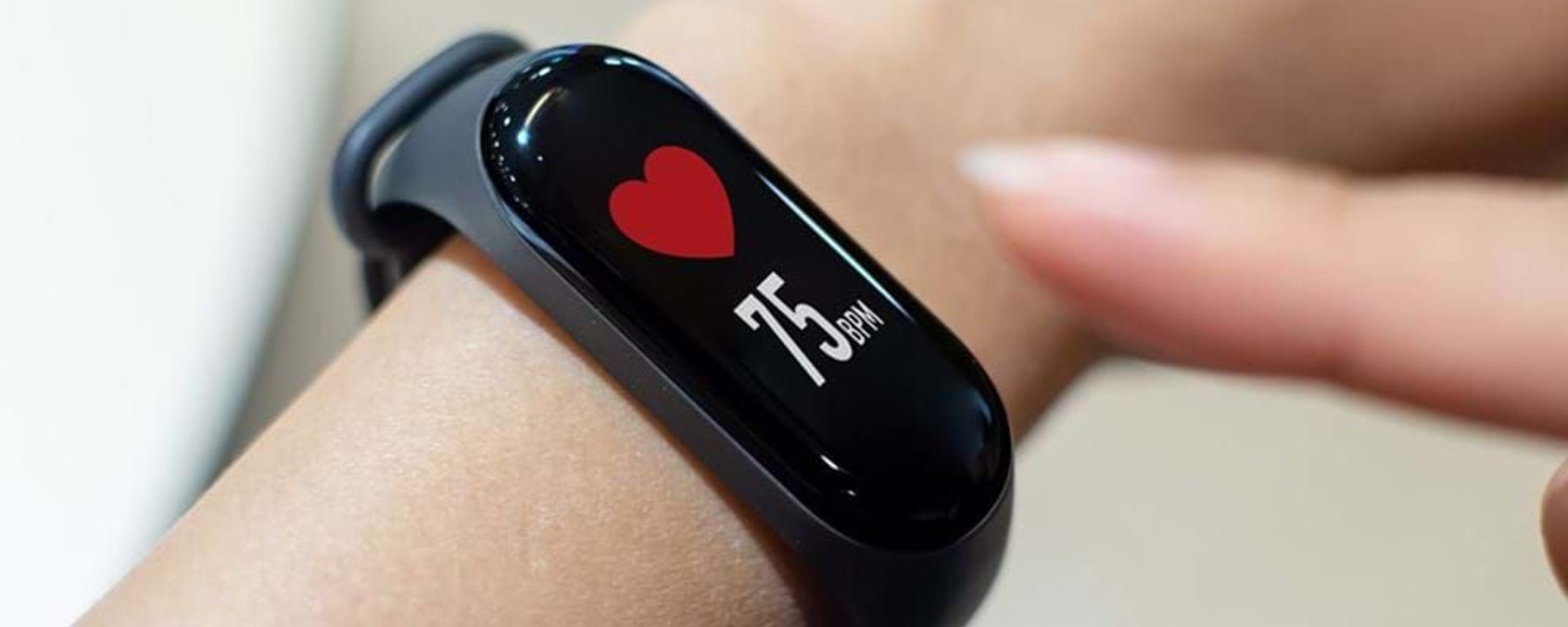 Fitness tracker on wrist showing heart rate of 75 bpm with finger pointing at it