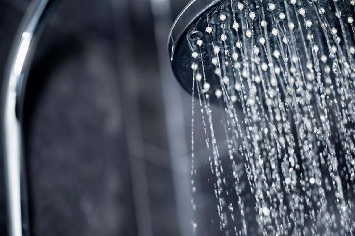 Water flowing from a round metal showerhead against a dark tiled wall