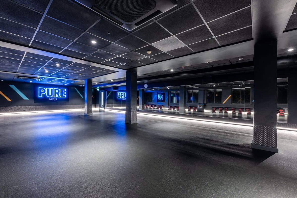 PureGym London Putney: Fitness studio with PURE Energy sign on the far wall, mirrors, and stacks of aerobic step platforms.