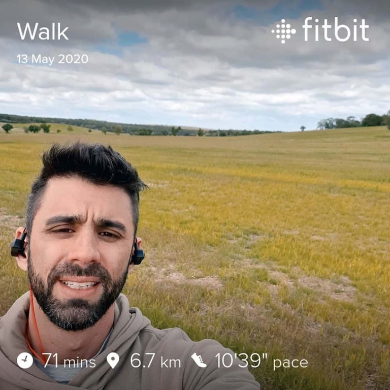 Man with earbuds in a field under a cloudy sky during a walk tracked by Fitbit