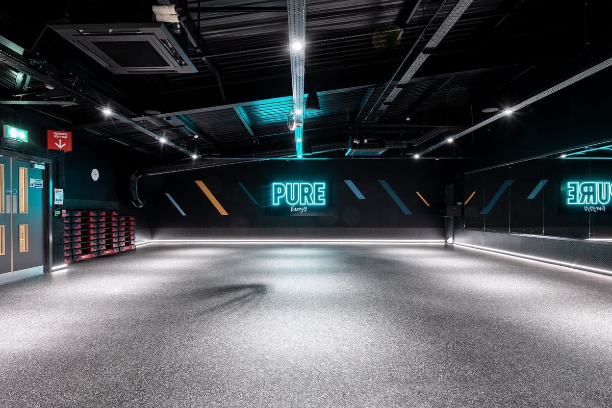 PureGym Cheshunt Brookfield Shopping Park: Dark futuristic gym studio with neon lights, rubberized floor and "PURE" signage.
