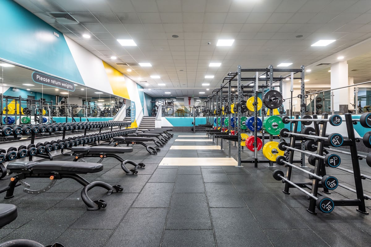 PureGym Harlow: Rows of resistance machines, free weights, benches, and mirrored walls in a bright, colorful gym.