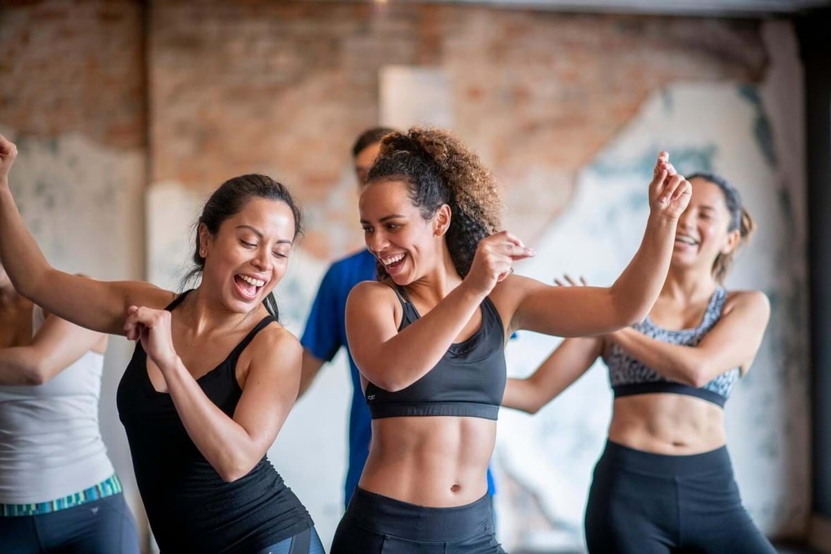 Group of women in sportswear dancing energetically indoors with smiles and raised arms