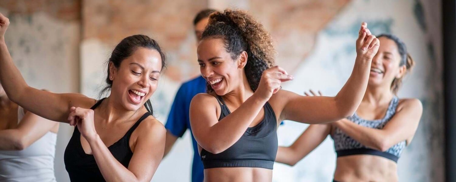 Group of women in sportswear dancing energetically indoors with smiles and raised arms