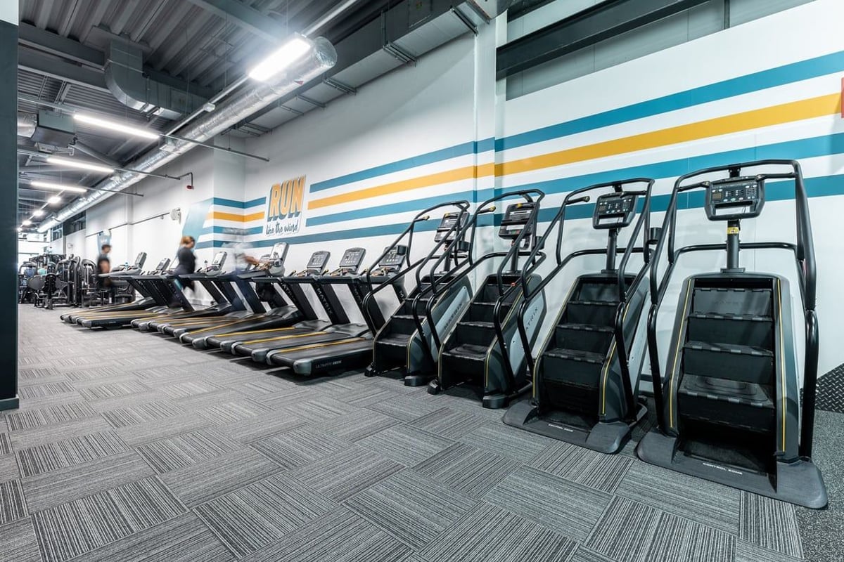 PureGym Chatham: Rows of treadmills lined up in a brightly lit gymnasium with striped walls.