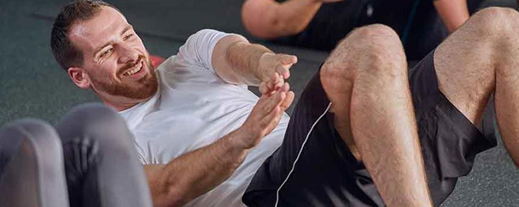 Homme en t-shirt blanc faisant des abdos au sol de la salle avec d’autres autour
