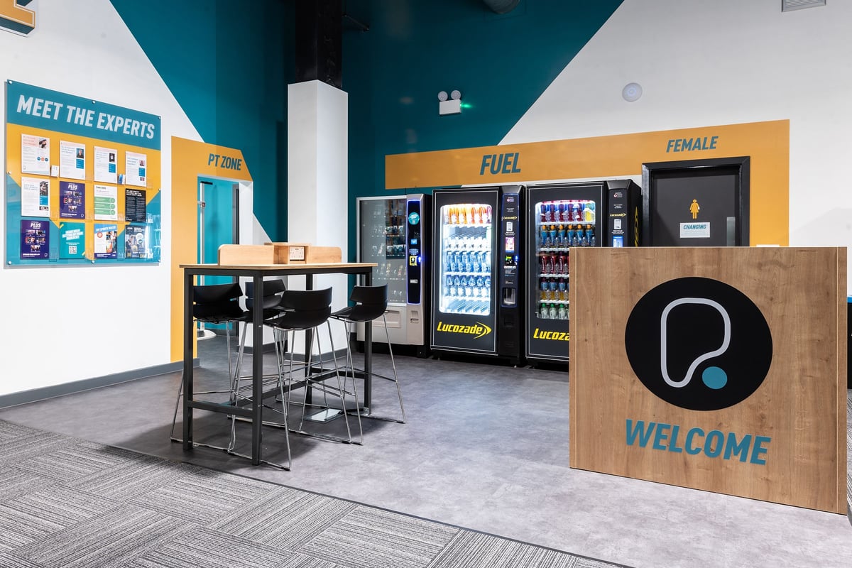 PureGym Bracknell: Vending machines, a meeting area with chairs and tables, and a welcome counter.