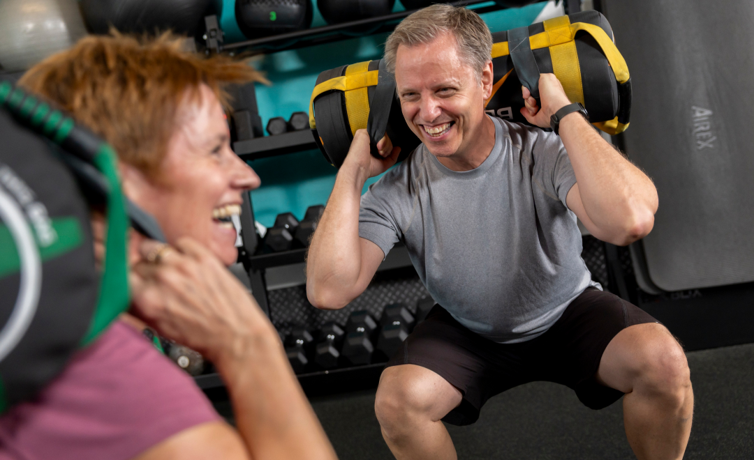 Mann hält gelbe und schwarze Kettlebells während des Trainings neben lächelnder Trainerin