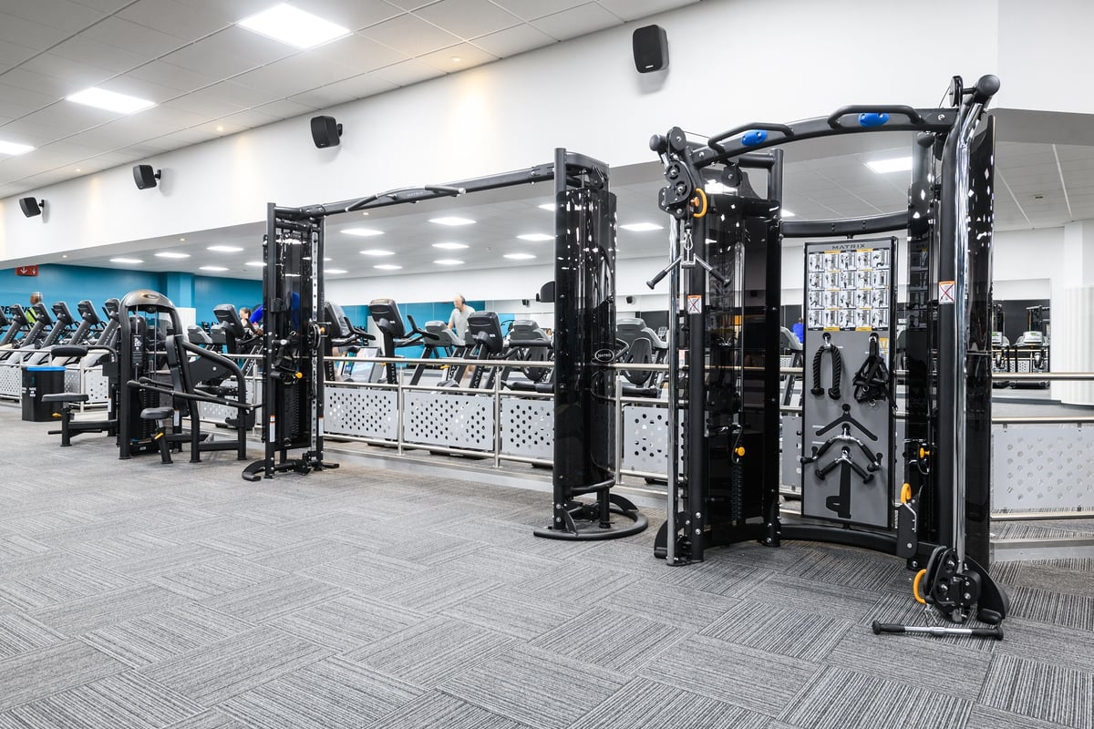 PureGym Aylesbury: Strength training rigs, weight plate storage, benches, and rubberized flooring in a gym space.