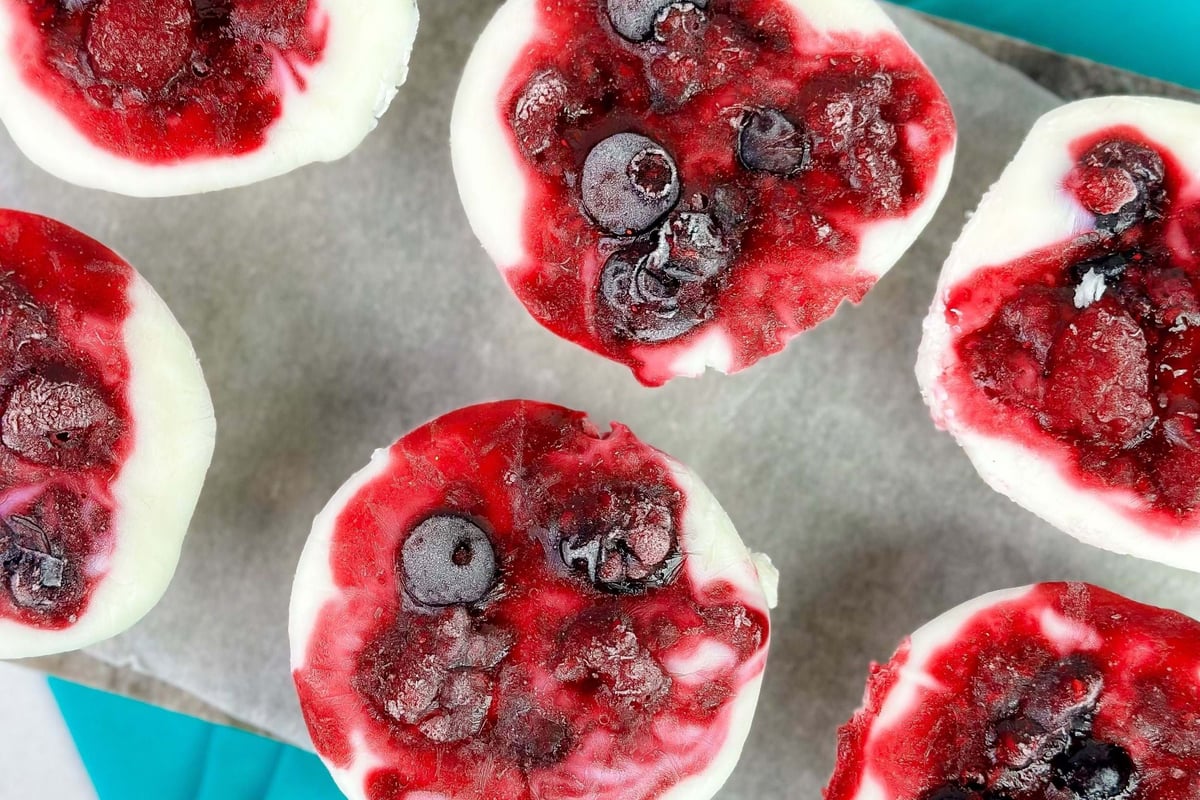 Frozen yoghurt cups topped with mixed berries on parchment and blue napkins