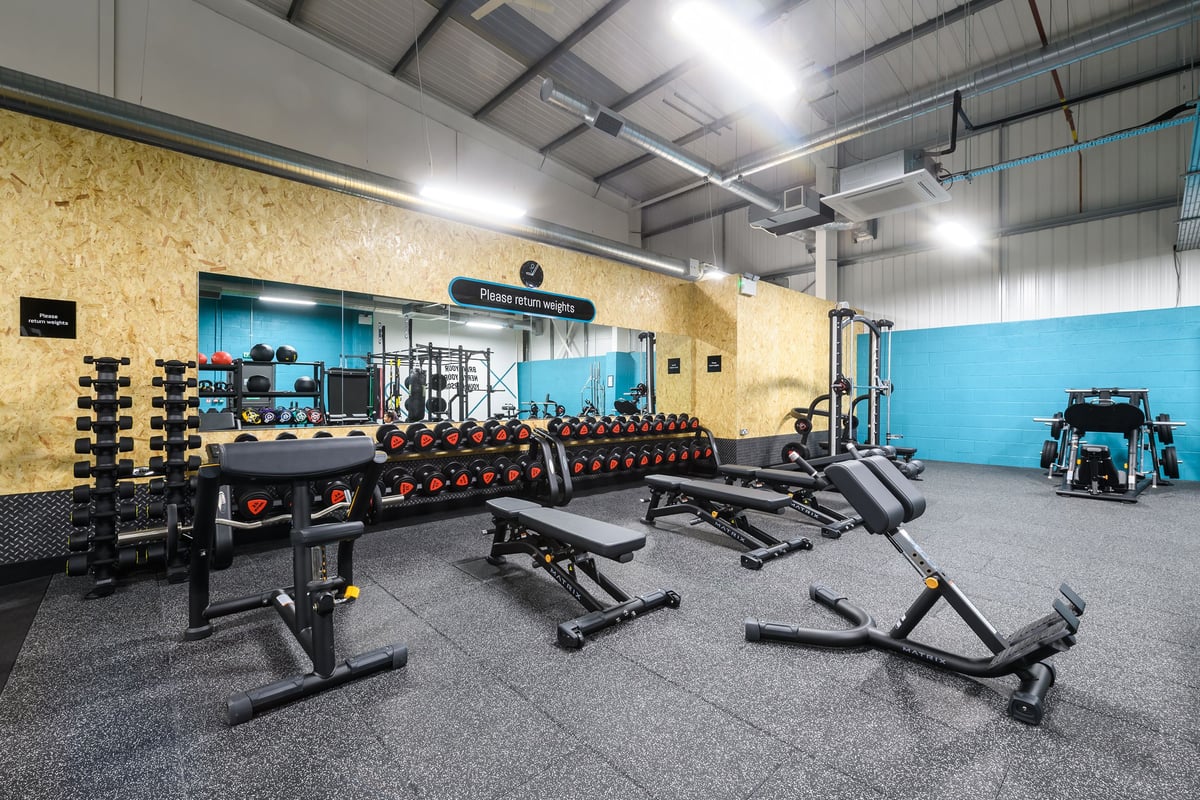 PureGym Buckingham: Workout floor with benches, weight racks, dumbbells, resistance bands, and rubberized flooring.