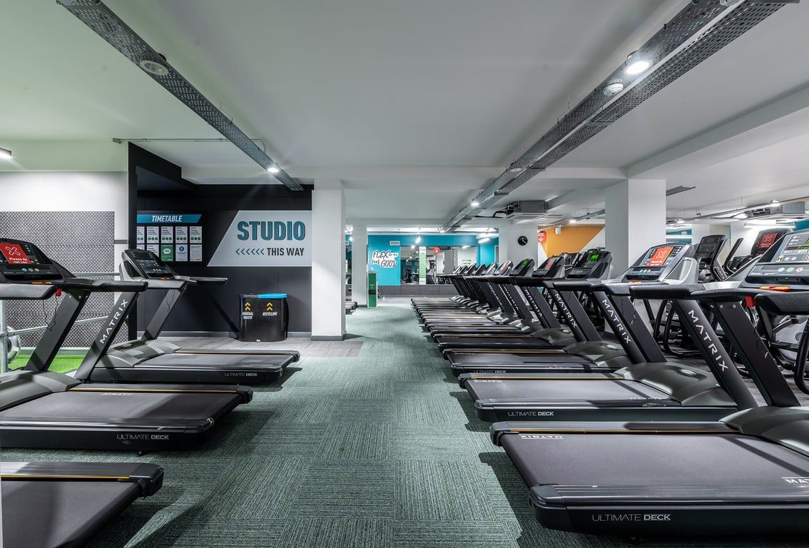 PureGym London Twickenham: Rows of treadmills, studio signage, and ventilation ducts in a modern fitness centre.