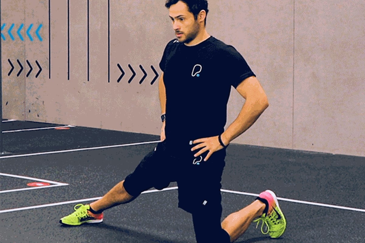 Man in black sportswear performing a kneeling lunge stretch on a gym floor