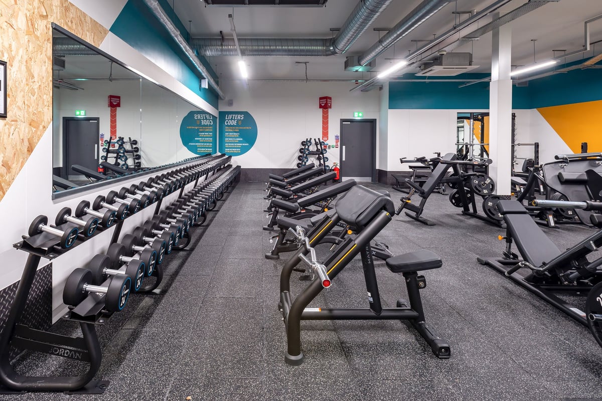PureGym Stratford-upon-avon: Rows of dumbbells, weight benches, and strength equipment in a modern gym interior.