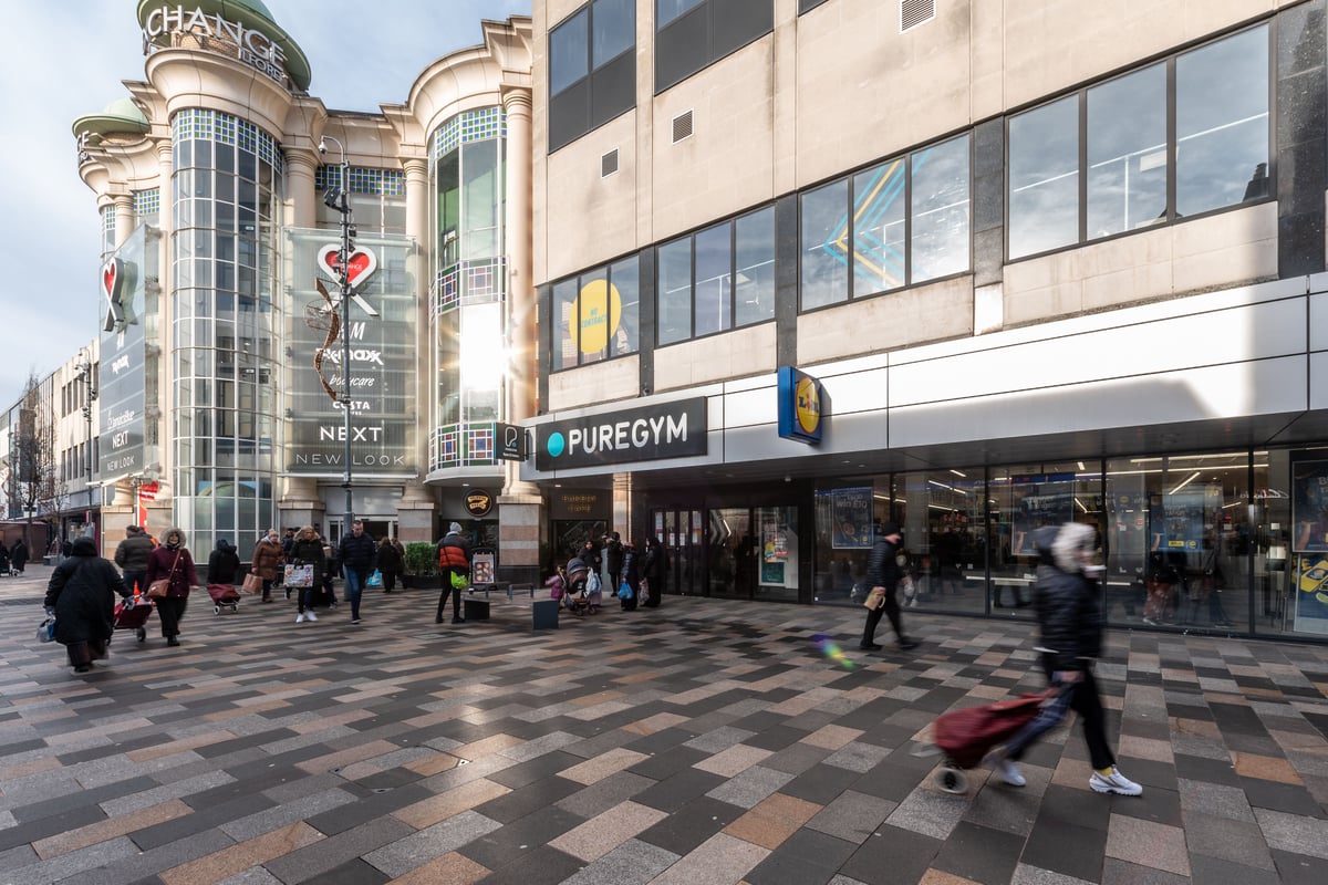 PureGym London Ilford: Gym signage and exterior of a shopping center with pedestrians walking by.