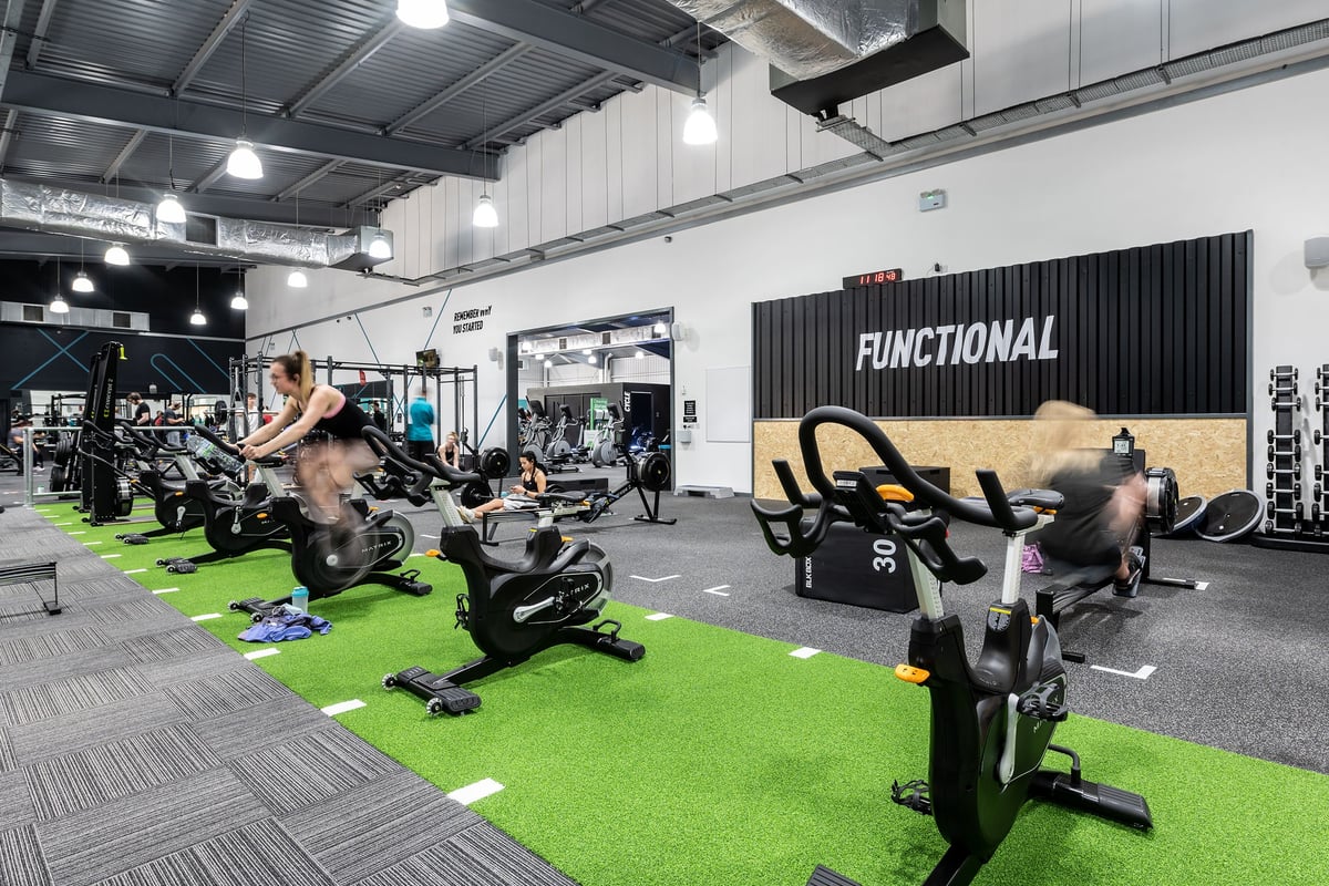 PureGym Warrington Central: Spin bikes, functional rigs, green turf area, free weights, mirrored wall in fitness studio.