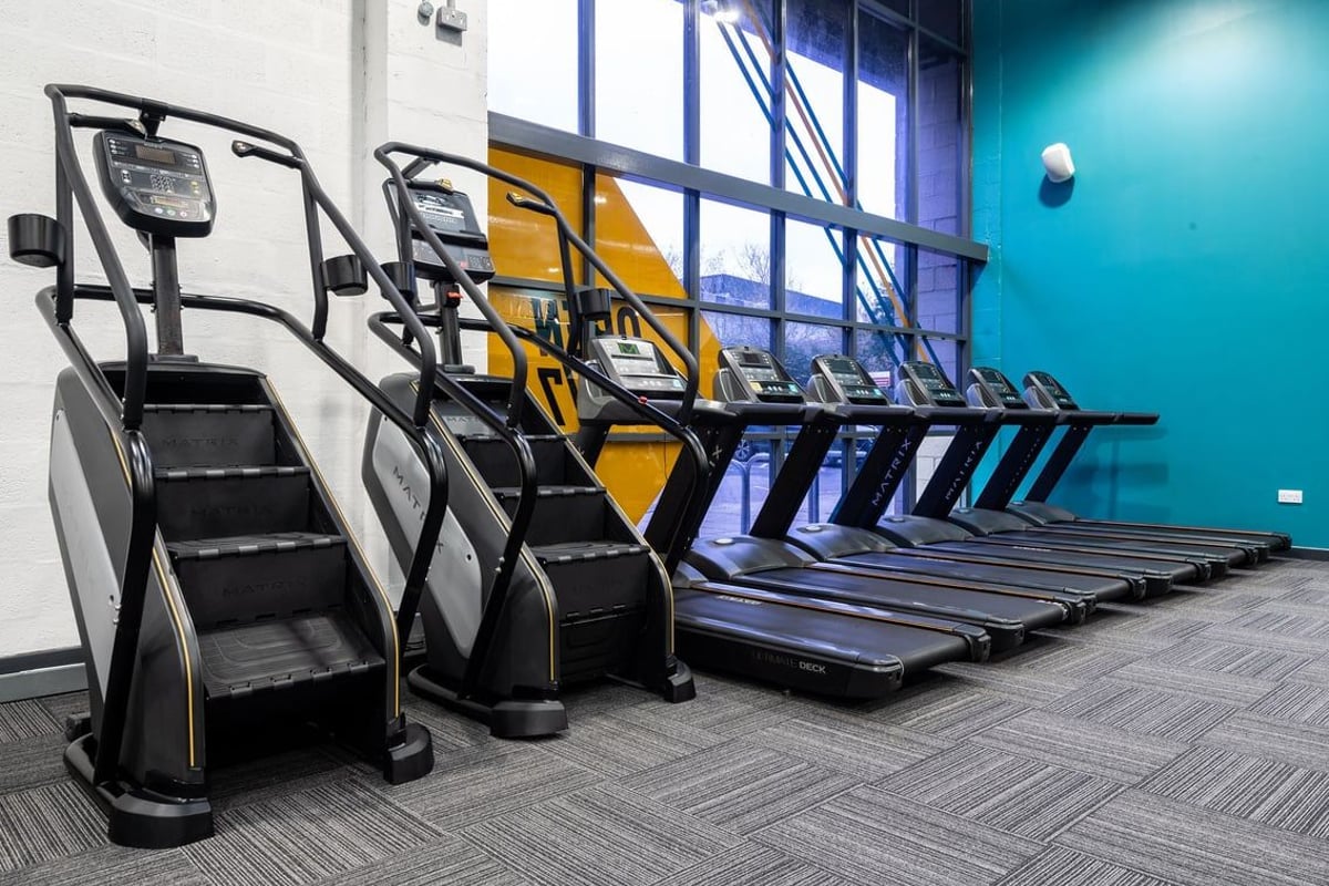 PureGym Dunfermline: Rows of treadmills and stair climbers in a modern gym setting with teal walls.