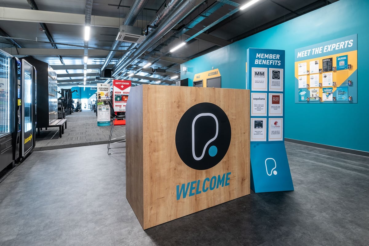 PureGym London Colney: Welcome area with signage, vending machines, and podium.