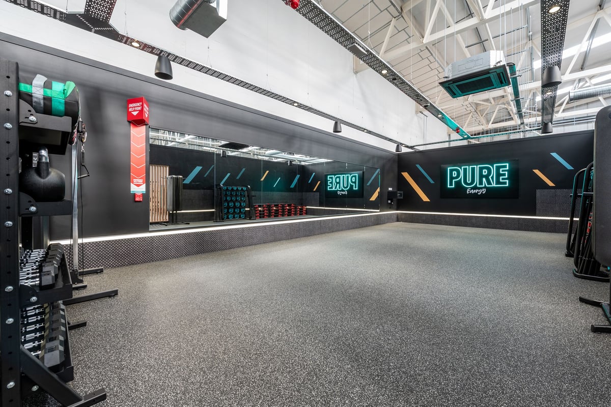 PureGym Bridgend: Bright studio space with neon signage, rubberized flooring, workout equipment.