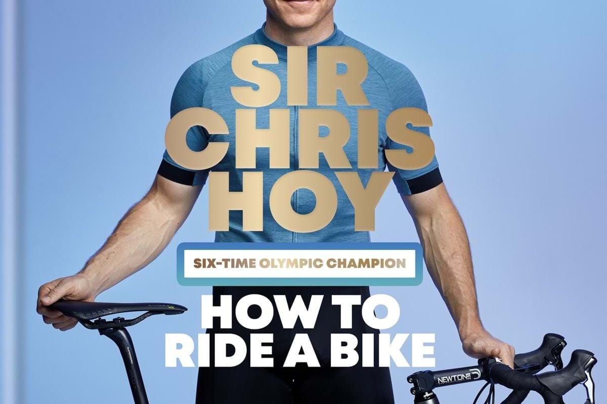 Man in cycling gear holding a white road bike against a blue background