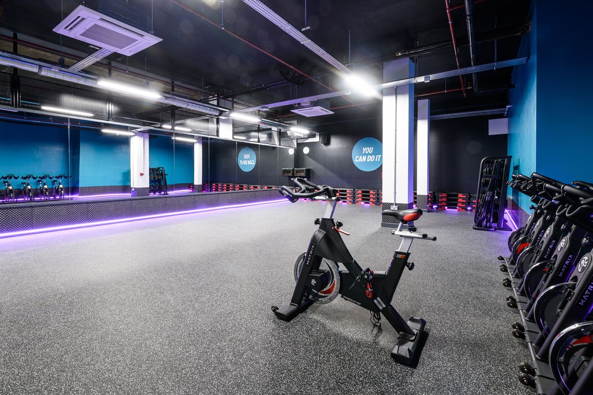 PureGym London Tottenham Court Road: Indoor cycling studio with stationary bikes, free weights, and teal-coloured accents.