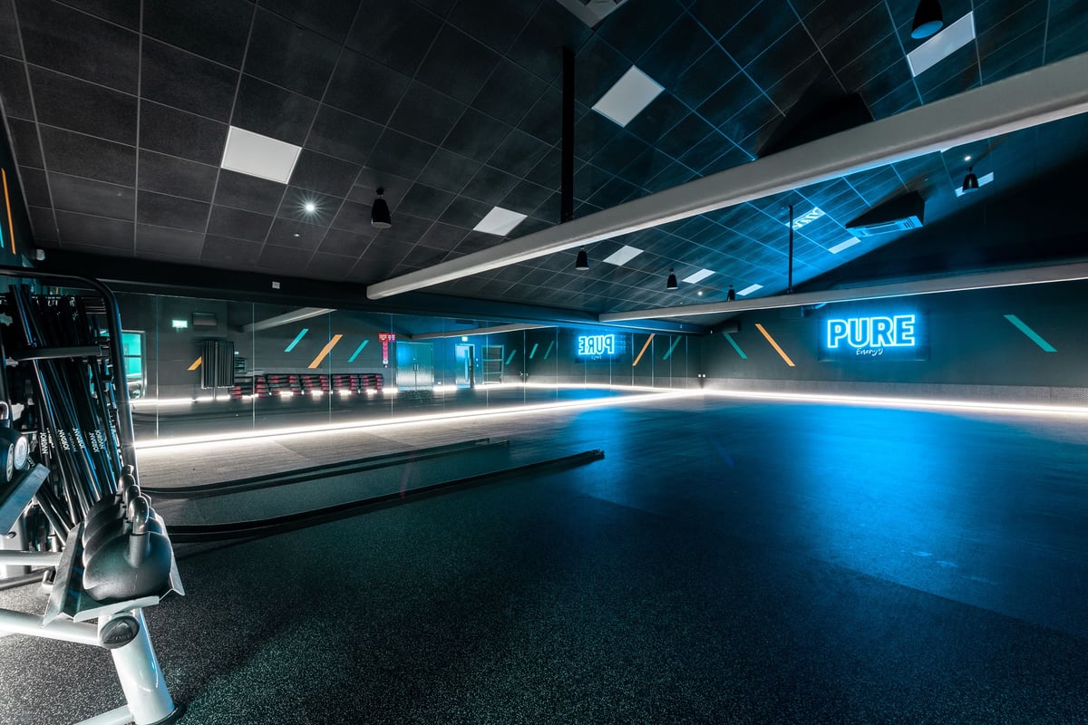 PureGym Bangor Northern Ireland: Futuristic gym interior with curved blue-lit running track and black ceiling grids.