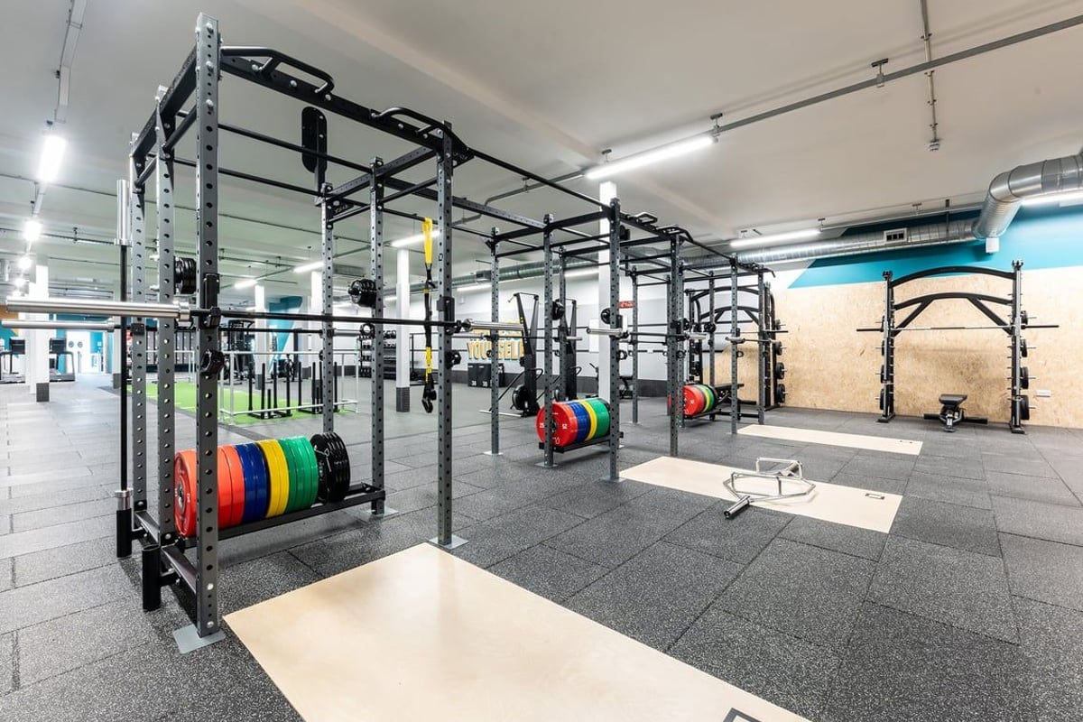 PureGym Shrewsbury Meole Brace: Weightlifting rig, weight plates, rubberized floors, mirrored walls in a spacious gym area.