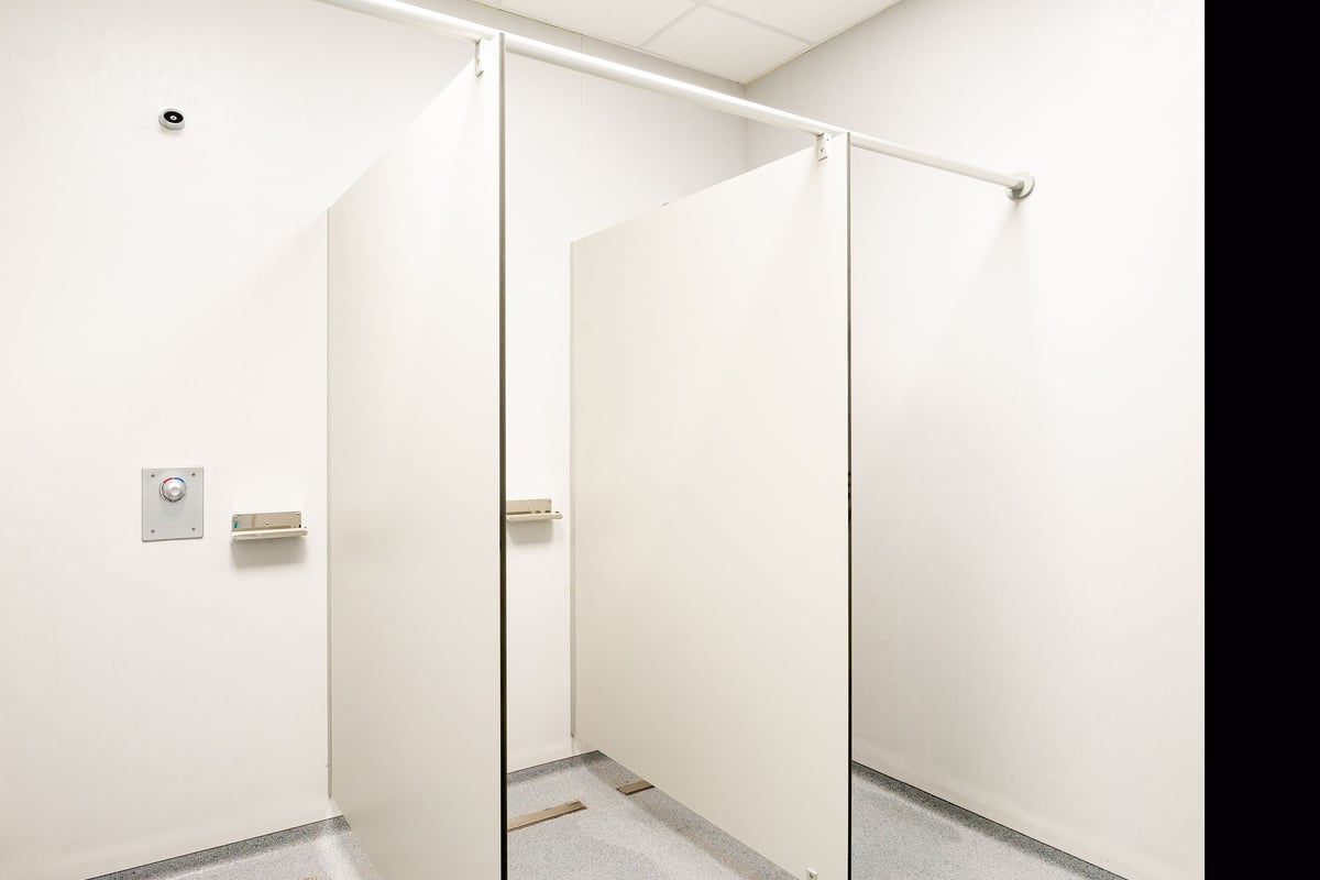 PureGym La Chaux-de-fonds: White-tiled changing room with floor-to-ceiling entry gates separating individual cubicles.