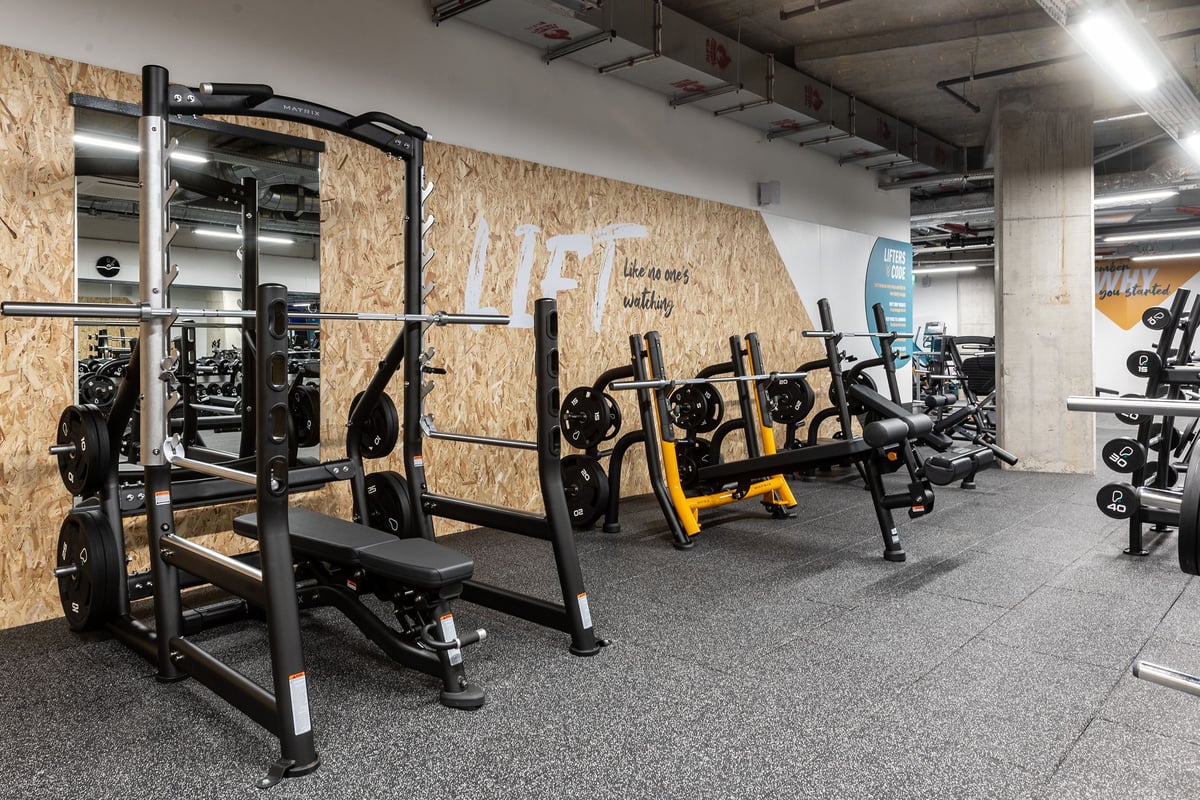 PureGym London Hoxton: Squat racks, benches, weight plates, rubberized floors in a gym setup with exposed wooden walls.