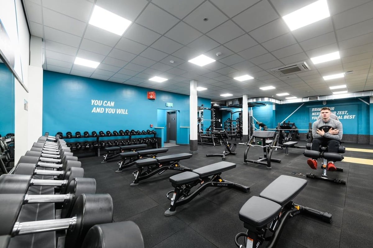 PureGym Lichfield: Rows of weight benches, dumbbell racks, and resistance machines in blue-toned gym studio.