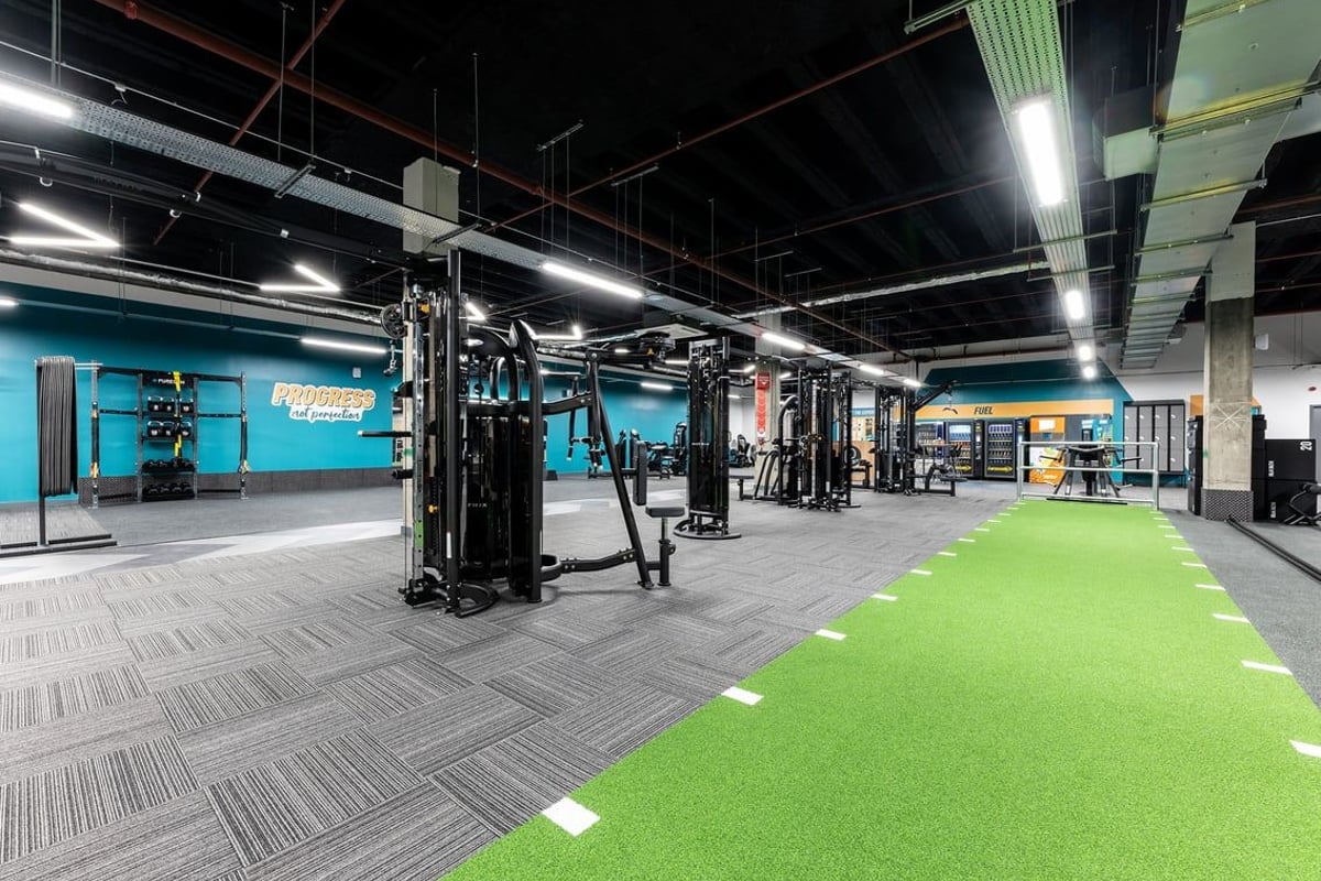PureGym London Stratford: Strength training area with cable machines, free weights, turf, and rubberized flooring.