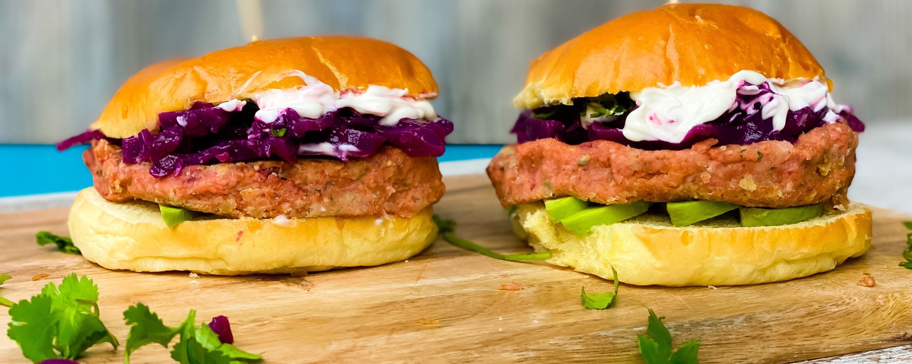 Two vegan burgers with breaded patties, purple cabbage and white sauce on wooden board