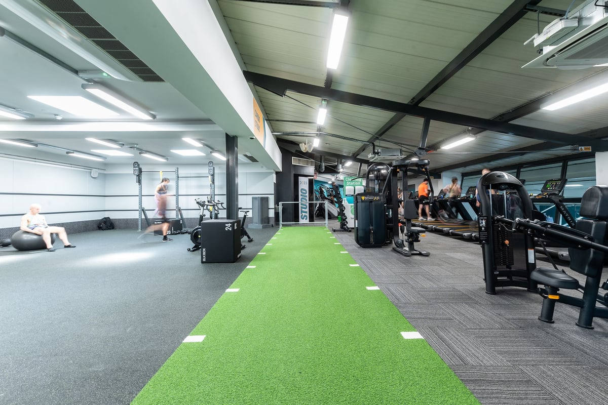 PureGym London Bayswater: Weights, machines, green turf area for training, fans on ceiling in a well-equipped gym interior.