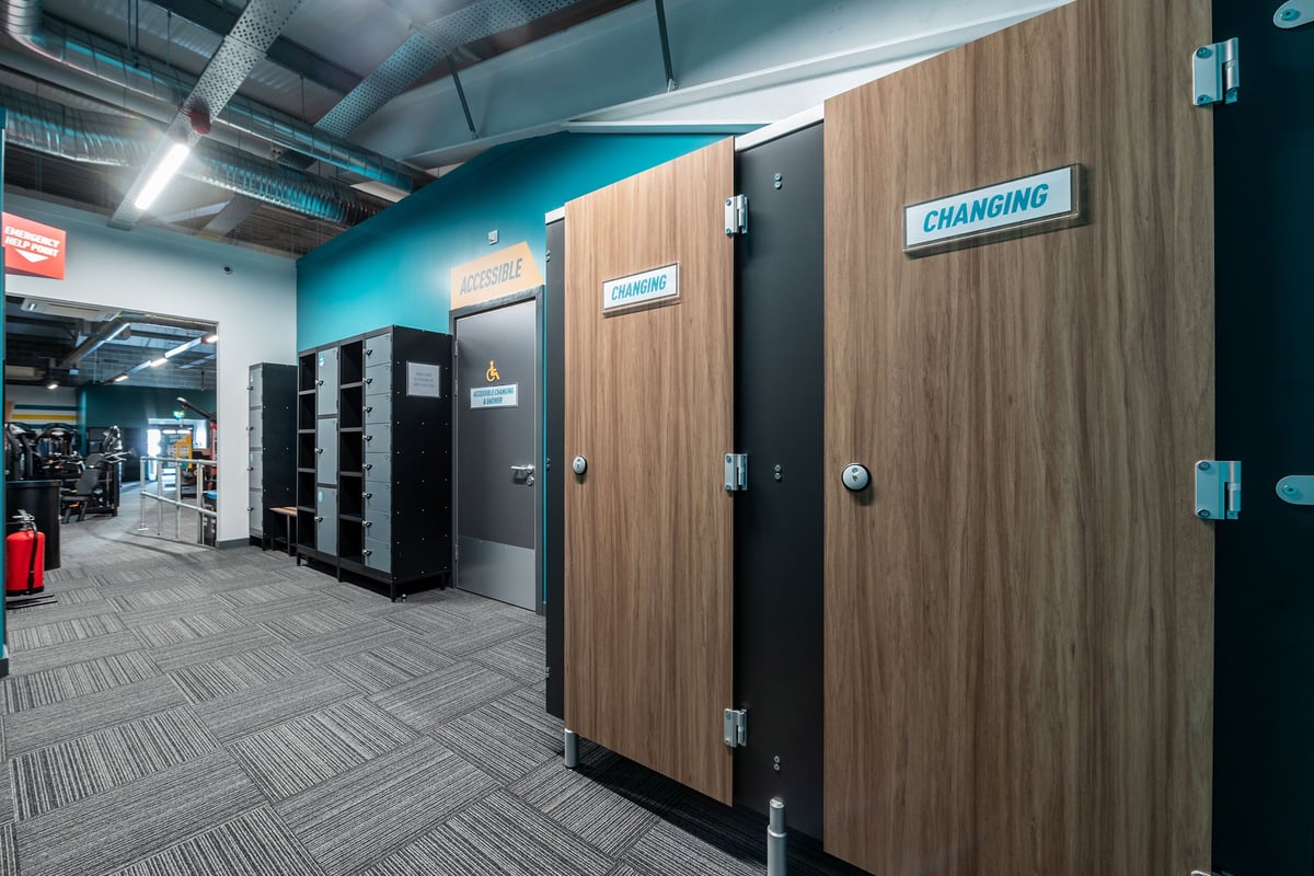 PureGym Aberdare: Rows of changing cubicles, wooden doors with 'Changing' signs, tiled flooring.