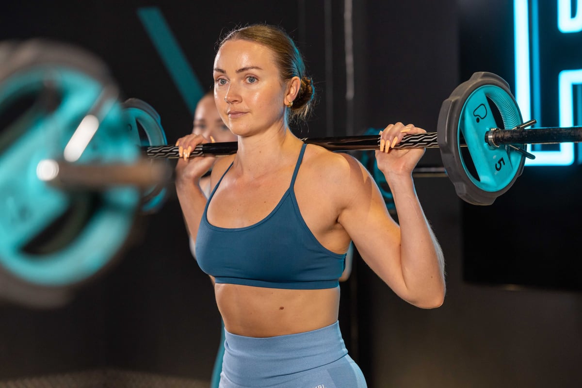 Woman lifting barbell weights in gym wearing blue sportswear