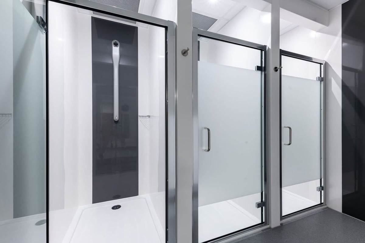 PureGym Caerphilly: Glass shower stalls, metal frames, and tiled flooring in changing room area.