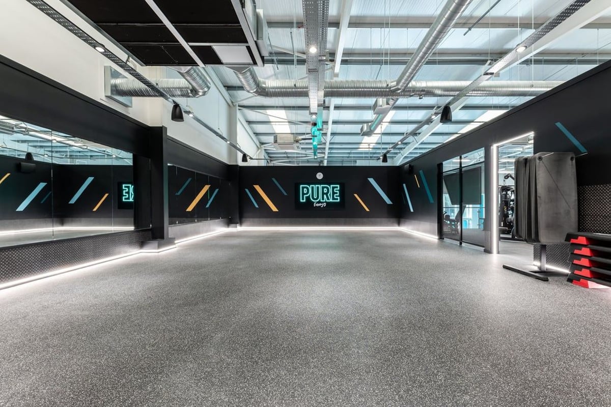 PureGym Caerphilly: Pristine gym studio with sleek black walls, neon lighting, and rubberized flooring.