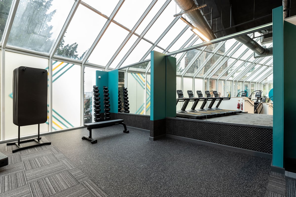 PureGym Ipswich Buttermarket: Glassed atrium gym with weight benches, dumbbells, resistance machines, and mirrored wall.