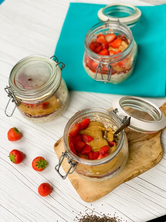 Three jars with overnight oats topped with peanut butter and strawberries on a white table