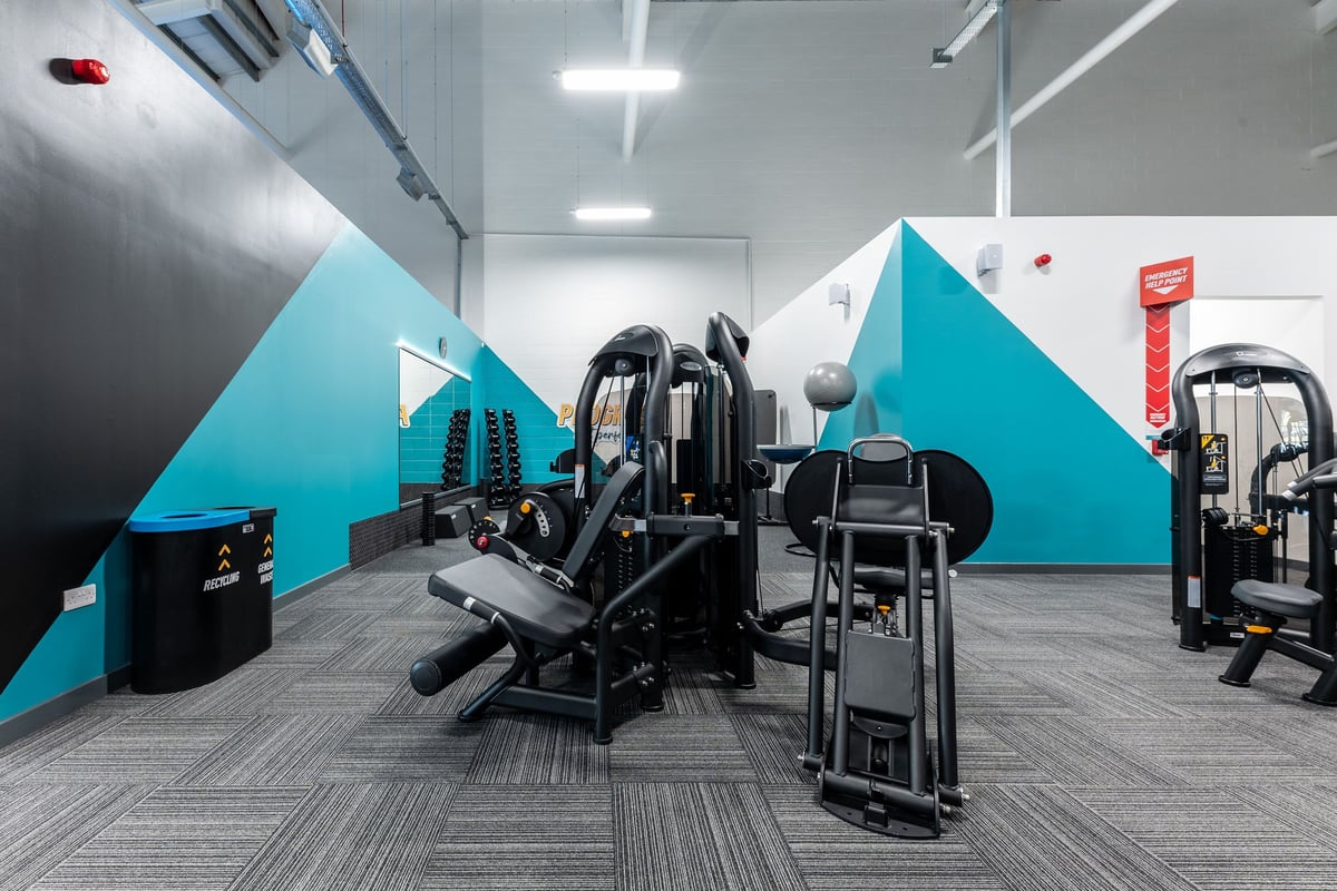PureGym Byfleet: Resistance machines, cable pulleys, benches, and rubberized flooring in a teal and grey gym studio.