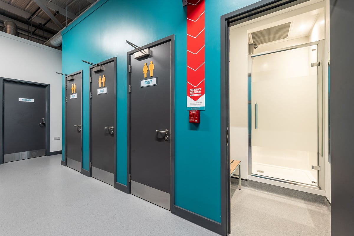 PureGym Bideford: Locker room with teal walls, black doors, and safety equipment mounted.