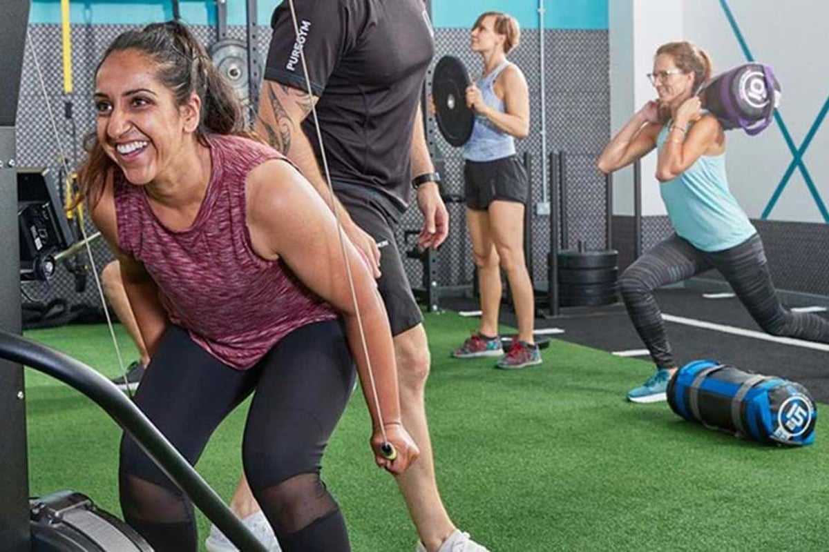 Femmes s'entraînant avec poids et câbles de résistance en salle, coach à proximité
