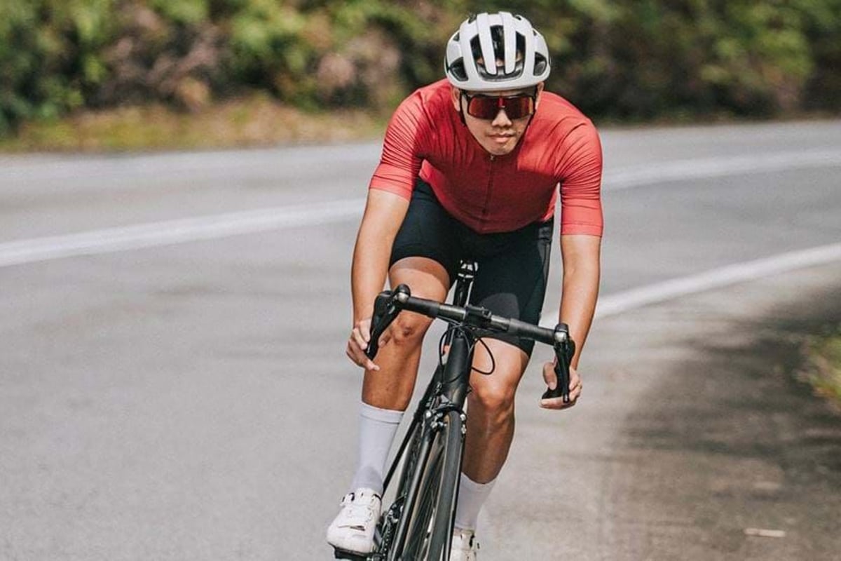 Cyclist wearing red jersey and white helmet riding a road bike on a curved road